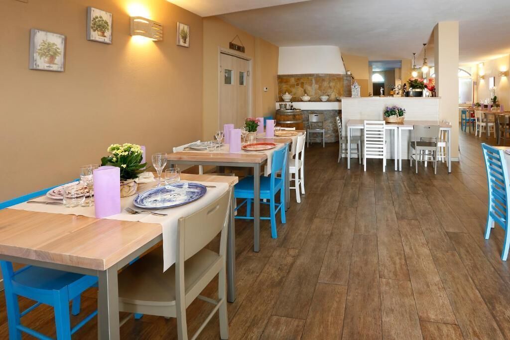 A dining area with wooden tables and blue chairs, a kitchen in the background, and a hallway leading to other rooms.