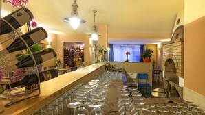 Zona de bar con varias botellas y copas de vino, un horno de piedra y vistas a la ciudad desde la ventana.