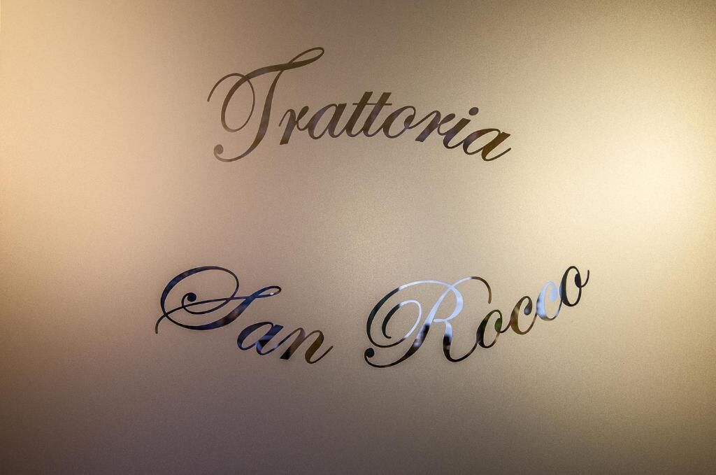 A wall with the text "Trattoria" and "San Rocco" in elegant script.