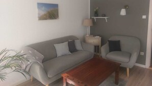 En stue med en grå sofa, et træ sofabord, en lampe og en lille plante.