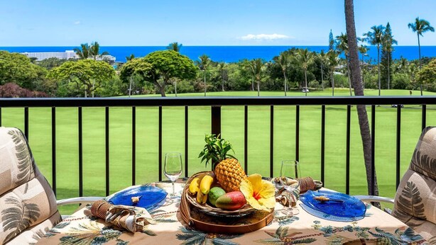 A table set with fruits and a tropical flower, overlooking a golf course and the ocean.
