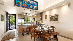 A modern kitchen with a large island, a dining area with wooden chairs, and a colorful fish mural on the ceiling.