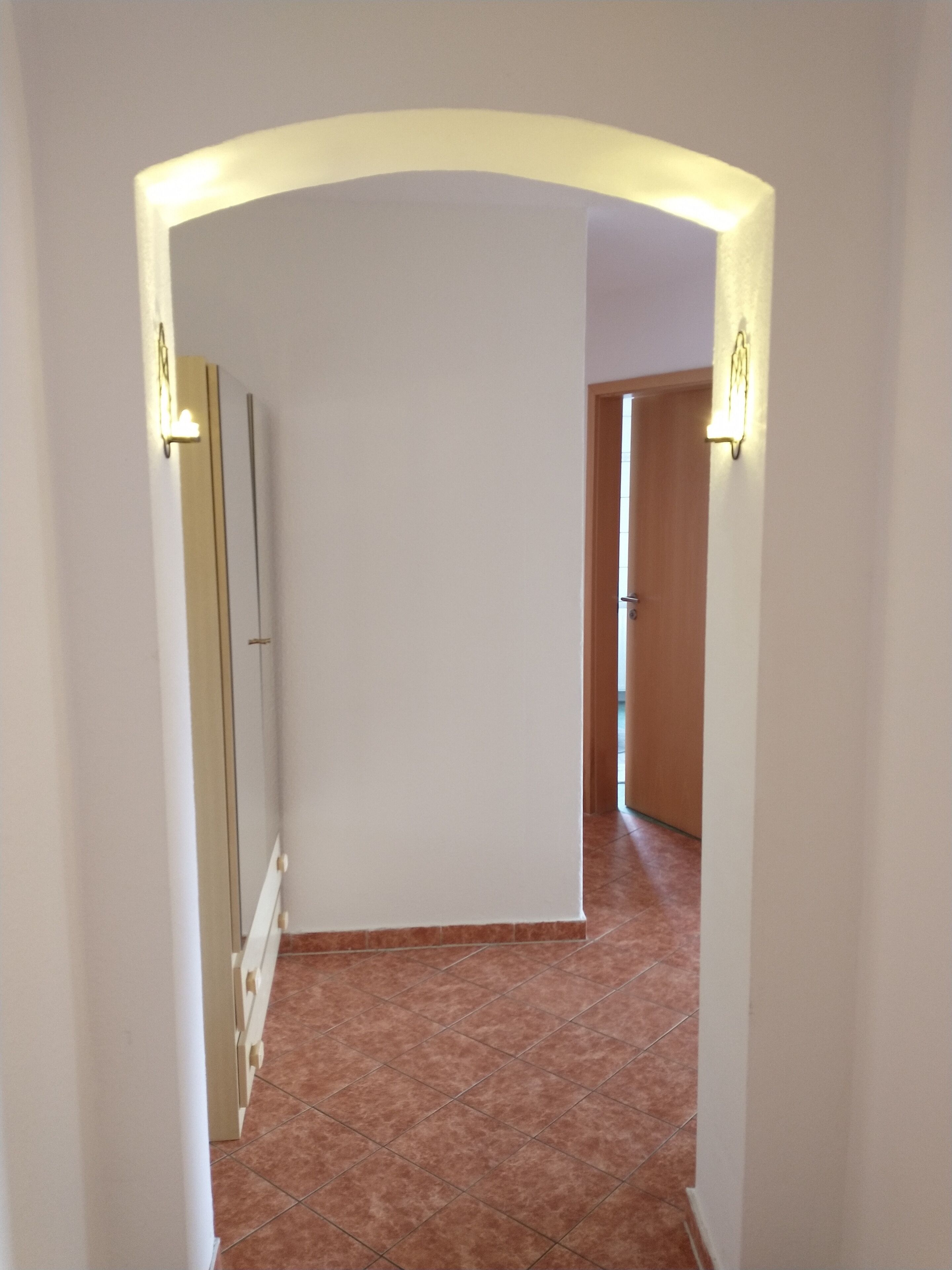 A hallway with a tiled floor, white walls, and a wooden door at the end.