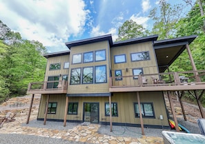A modern two-story house with a balcony, stone patio, and a hot tub.