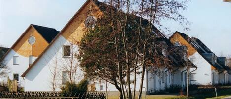 A row of white houses with wooden gable roofs and a tree in the foreground.