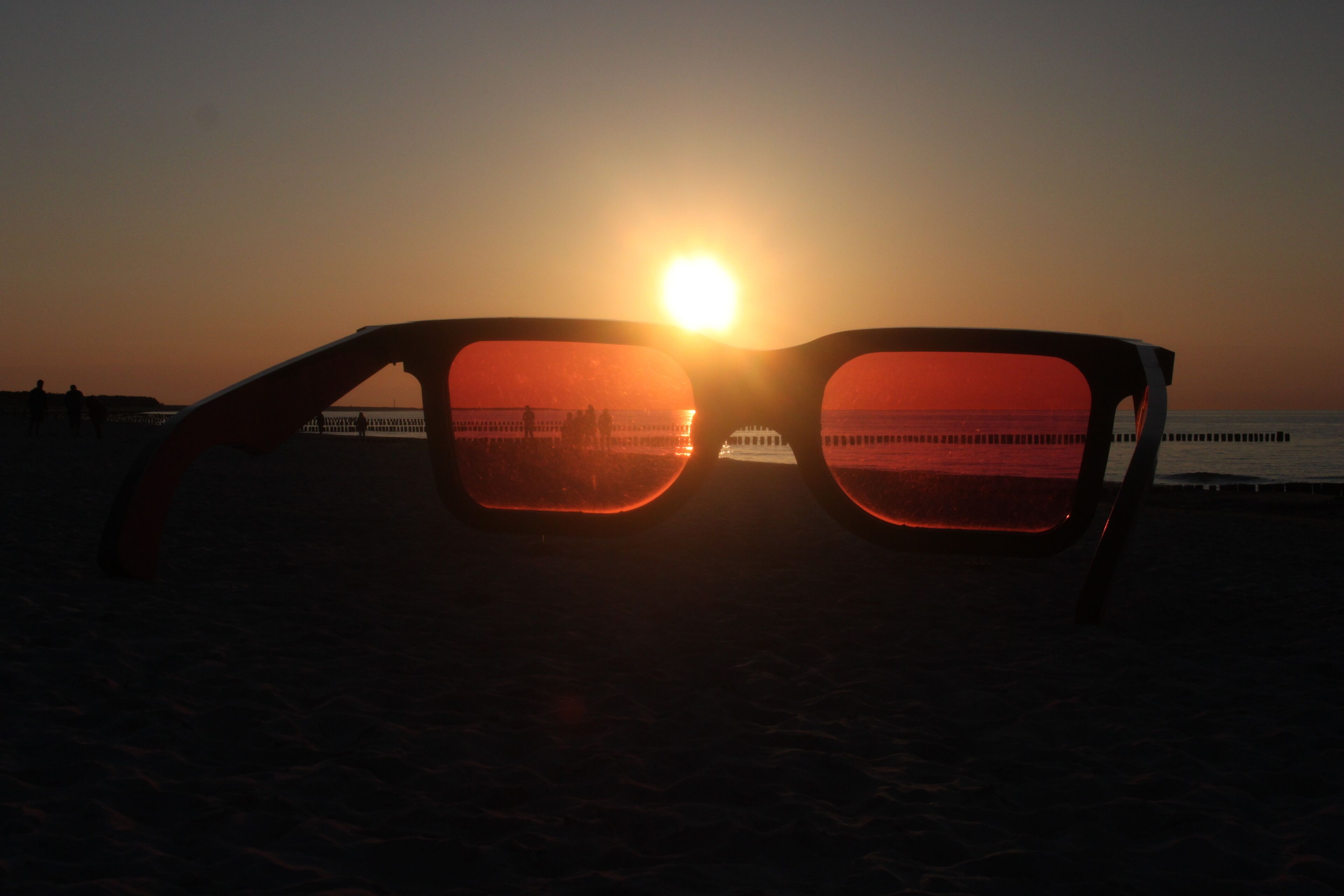 A pair of sunglasses with a sunset reflected in the lenses.