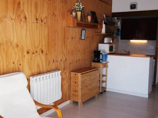 A compact kitchen with wooden walls, a white refrigerator, a microwave, and a small wooden table with a coffee maker.