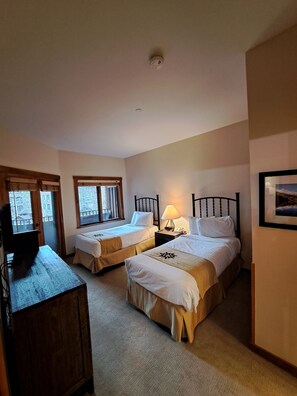 Ein Hotelzimmer mit zwei Betten, einem Schreibtisch, einem Fernseher und einem Fenster mit Jalousien.