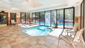Amplia zona de piscina interior con vistas a una cascada y una piscina exterior.