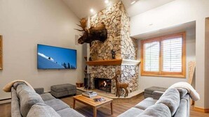 Una sala de estar con chimenea de piedra, cabeza de alce montada y televisor en la pared.