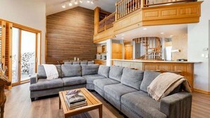 Un salón amplio con un sofá modular grande, una escalera de madera y una zona de cocina.
