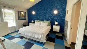 Ein modernes Schlafzimmer mit Schachbrettmuster-Boden, einem Bett mit weißer Bettwäsche, einem Nachttisch mit Lampe und einem Deckenventilator.