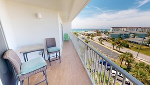 Een balkon met rieten meubilair, uitzicht op het strand en een parkeerplaats.