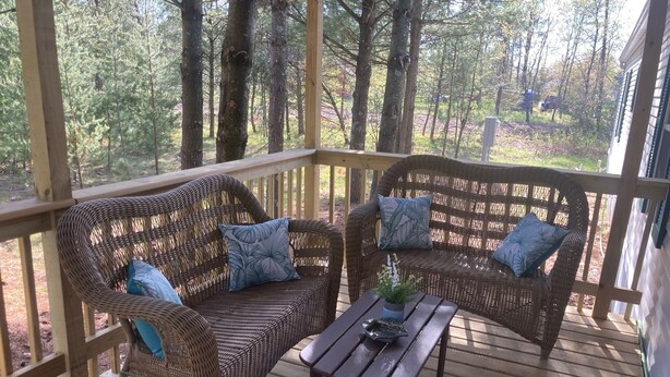 Un espacio de estar al aire libre cubierto con muebles de mimbre y una mesa de madera, rodeado de árboles.