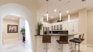 A modern kitchen with white cabinets, a central island with bar stools, pendant lighting, and a framed picture on the wall. - Villas House Bayview 3 Bedroom Home by RedAwning (South Padre Island)