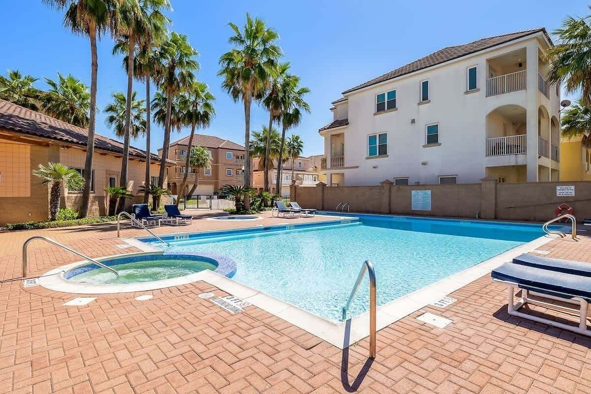 A swimming pool with lounge chairs and palm trees, surrounded by buildings with balconies.