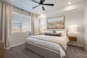 A bedroom with a bed, a ceiling fan, a nightstand with a lamp, and a painting on the wall. - Blue Sky Oasis 2 Bedroom Condo (St. George)