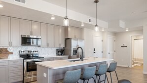 A modern kitchen with stainless steel appliances, a central island with bar stools, and pendant lighting. - Blue Sky Oasis 2 Bedroom Condo (St. George)