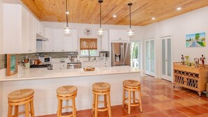 Una cucina moderna con mobili bianchi, una grande isola con sgabelli, elettrodomestici in acciaio inossidabile e soffitto in legno.