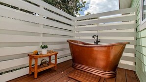 Un terrazzo in legno con una vasca da bagno in rame, un piccolo tavolo di legno con una pianta e una panca.