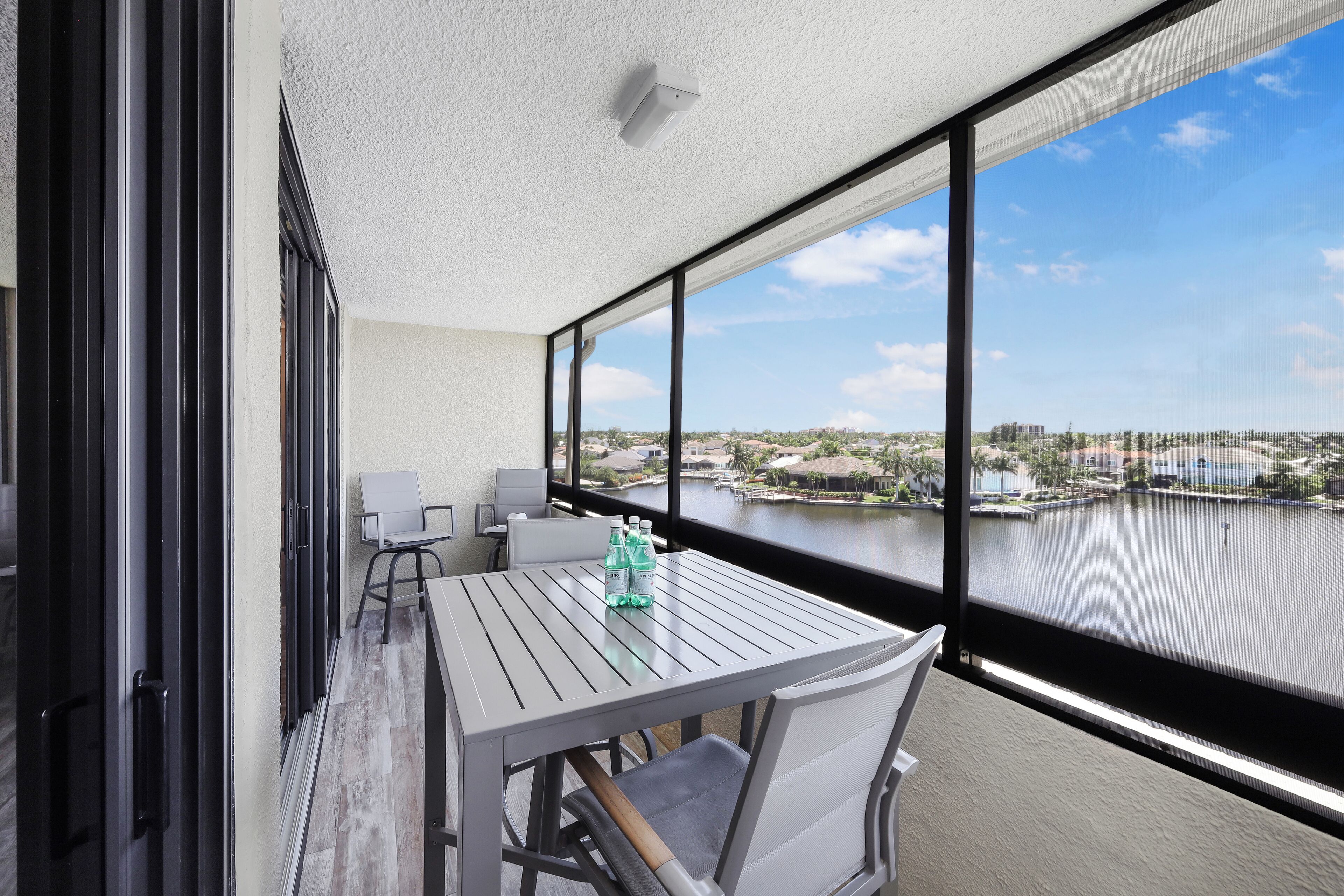 Un balcon avec une table, des chaises et une vue sur un plan d’eau et des bâtiments.
