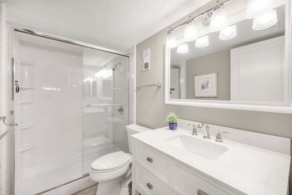 A modern bathroom with a glass-enclosed shower, a white toilet, a vanity with a sink, and a mirror with lights.