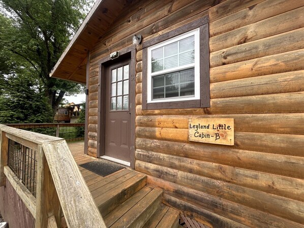 Een houten hutje met een bruine deur en een raam, met de tekst 'Leyland Little Cabin-B'.