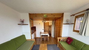 A cozy living room with a wooden table, two green sofas, a wooden dining table, and a kitchen area visible through an open doorway. - 100m from ski slopes, 2nd floor, view ski slopes, balcony, tv, ski locker, 23m², Les Saisies (Les Saisies)