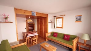 A cozy living room with a green sofa, wooden coffee table, and a dining area with a striped tablecloth. - 100m from ski slopes, 2nd floor, view ski slopes, balcony, tv, ski locker, 23m², Les Saisies (Les Saisies)
