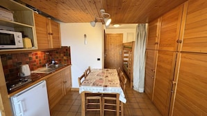 A compact kitchen with wooden cabinets, a tiled floor, a dining table with chairs, and a white refrigerator. - 100m from ski slopes, 2nd floor, view ski slopes, balcony, tv, ski locker, 23m², Les Saisies (Les Saisies)