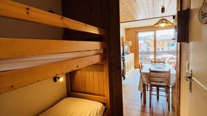 Quarto com beliches, teto de madeira e vista para o exterior por uma porta aberta.