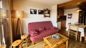 Uma sala de estar aconchegante com um sofá vermelho estampado, uma mesa de centro de madeira e uma área de jantar com mesa e cadeiras.