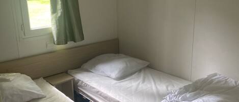 A small, compact room with two single beds, a window with a curtain, and a wooden headboard.