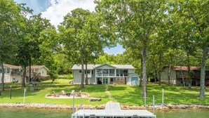 Une propriété au bord du lac comprenant une maison, un quai et un espace extérieur aménagé pour s’asseoir.
