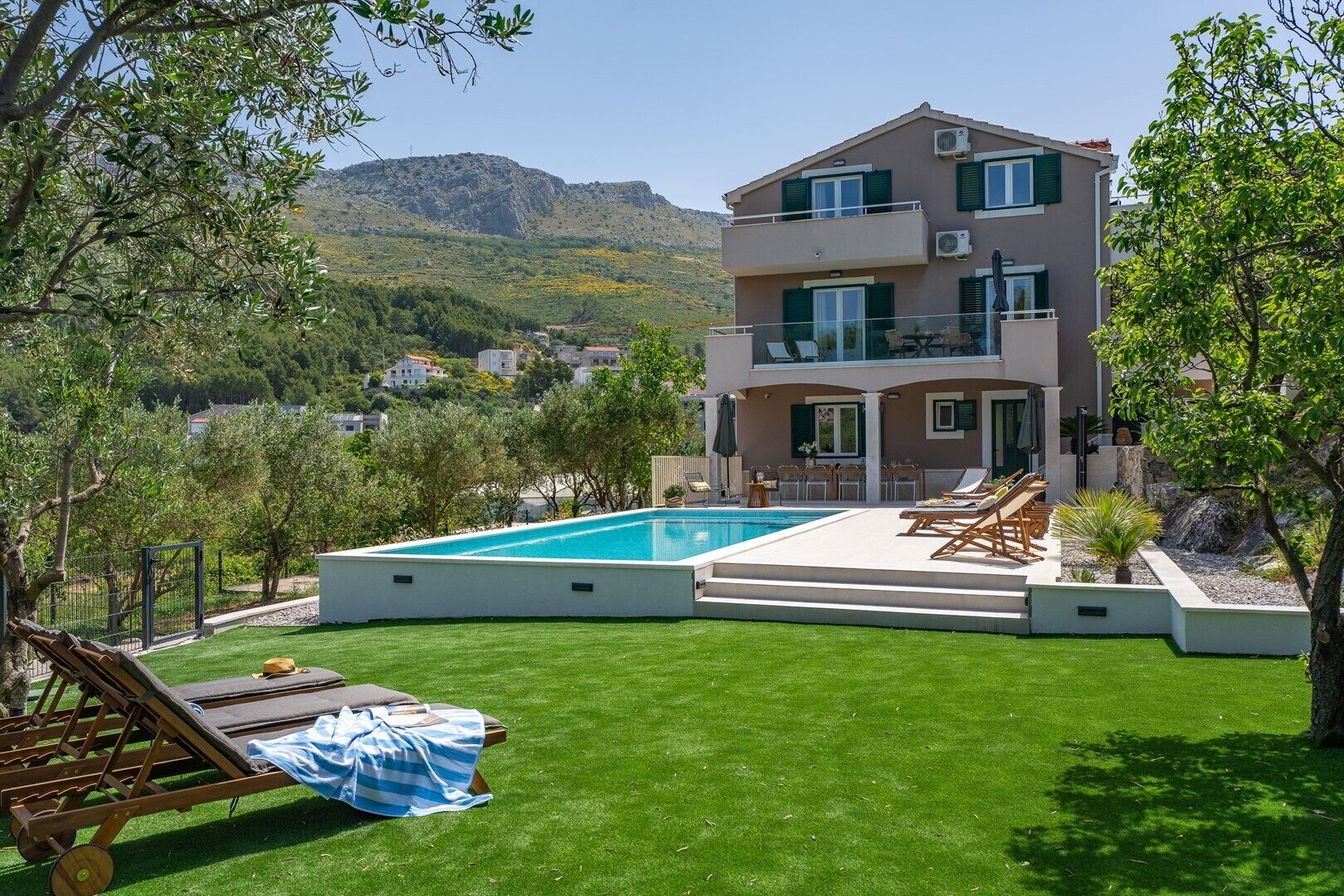 A two-story house with a swimming pool, outdoor seating, and a view of hills.