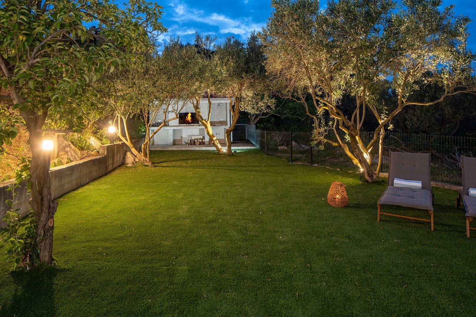 A well-maintained backyard with a grassy lawn, a barbecue area, and two lounge chairs.