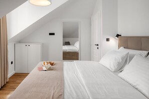 Ein modernes Schlafzimmer mit schrägen Wänden, einem Bett mit weißer Bettwäsche, einem Nachttisch mit Buch und Gebäck sowie einem Kleiderschrank.