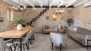 A spacious living area with a wooden dining table, sofas, and a staircase against a stone wall.