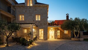A stone building with multiple windows, a covered patio area with outdoor seating, and a red-tiled roof.