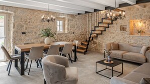 A spacious living room with a stone wall, a wooden staircase, and a dining area with modern furniture.