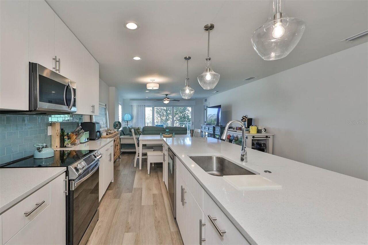 A modern kitchen with white cabinetry, stainless steel appliances, and pendant lighting.