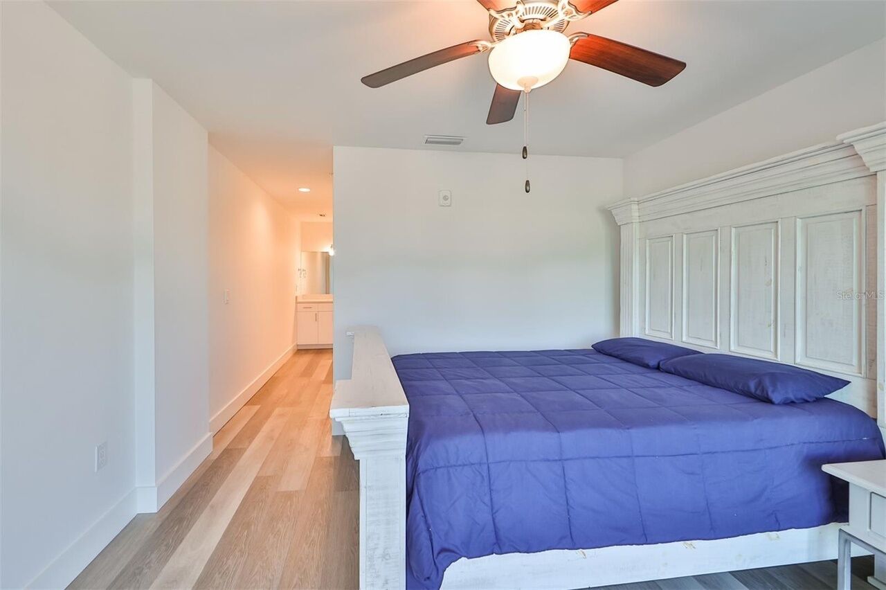 A bedroom with a bed, a ceiling fan, and a nightstand.