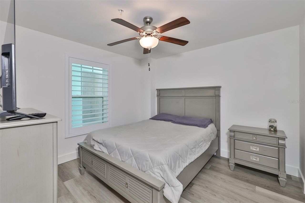 A bedroom with a bed, a nightstand, a TV, and a ceiling fan.