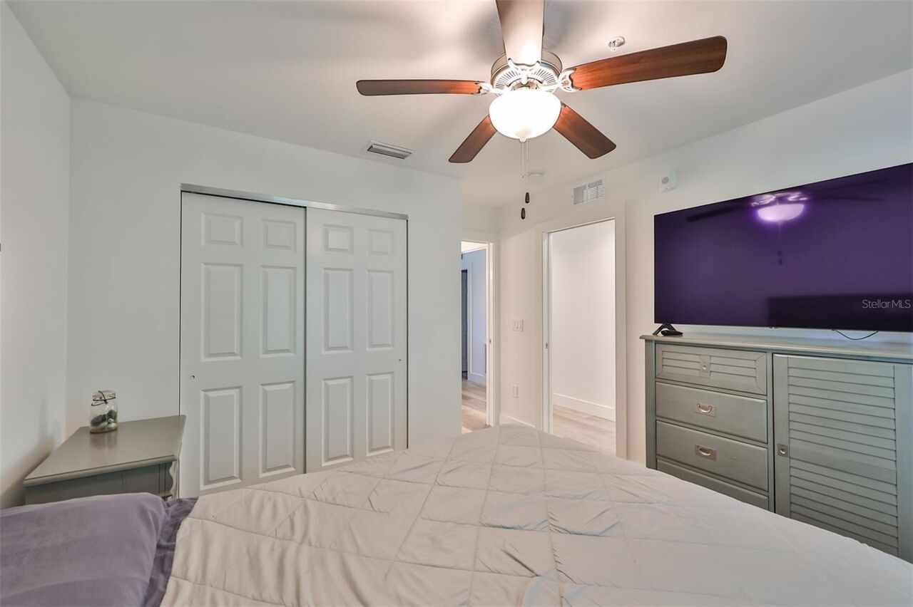 A bedroom with a bed, a ceiling fan, a TV, and a dresser.