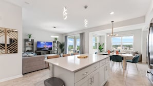 A modern kitchen with a central island, a dining area, and a living space with a sofa and TV.