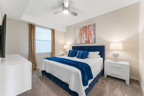 A bedroom with a bed, nightstands, a ceiling fan, a TV, and a window with curtains.