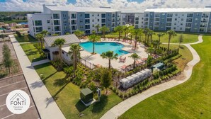A modern hotel with a central pool surrounded by palm trees and outdoor seating.