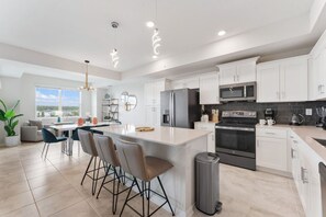 A modern kitchen with white cabinets, a central island with bar stools, stainless steel appliances, and a view of the outdoors. - 3171-302 Resort Lake View Disney Universal Orlando (Kissimmee)
