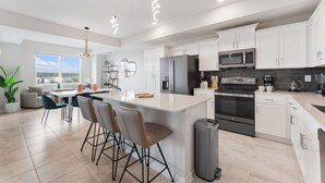 A modern kitchen with white cabinets, a central island with bar stools, stainless steel appliances, and a view of the outdoors.