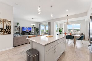 A modern kitchen with a central island, a dining area, and a living space with a sofa and TV. - 3171-302 Resort Lake View Disney Universal Orlando (Kissimmee)
